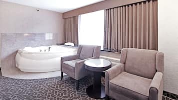A modern bathroom with a large bathtub, two armchairs, and a round table.