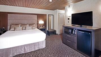 Ein Hotelzimmer mit einem großen Bett, einem Flachbildfernseher, einer Minibar und einem kleinen Hocker.