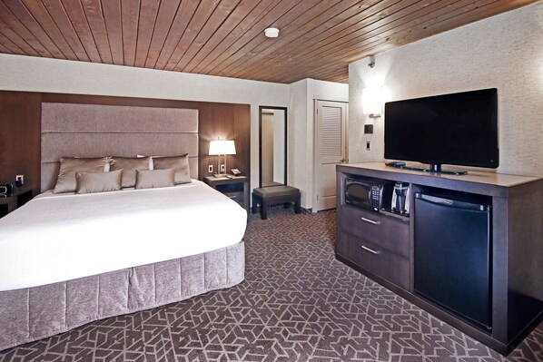 Une chambre d’hôtel avec un grand lit, un téléviseur à écran plat, un minibar et un petit tabouret.