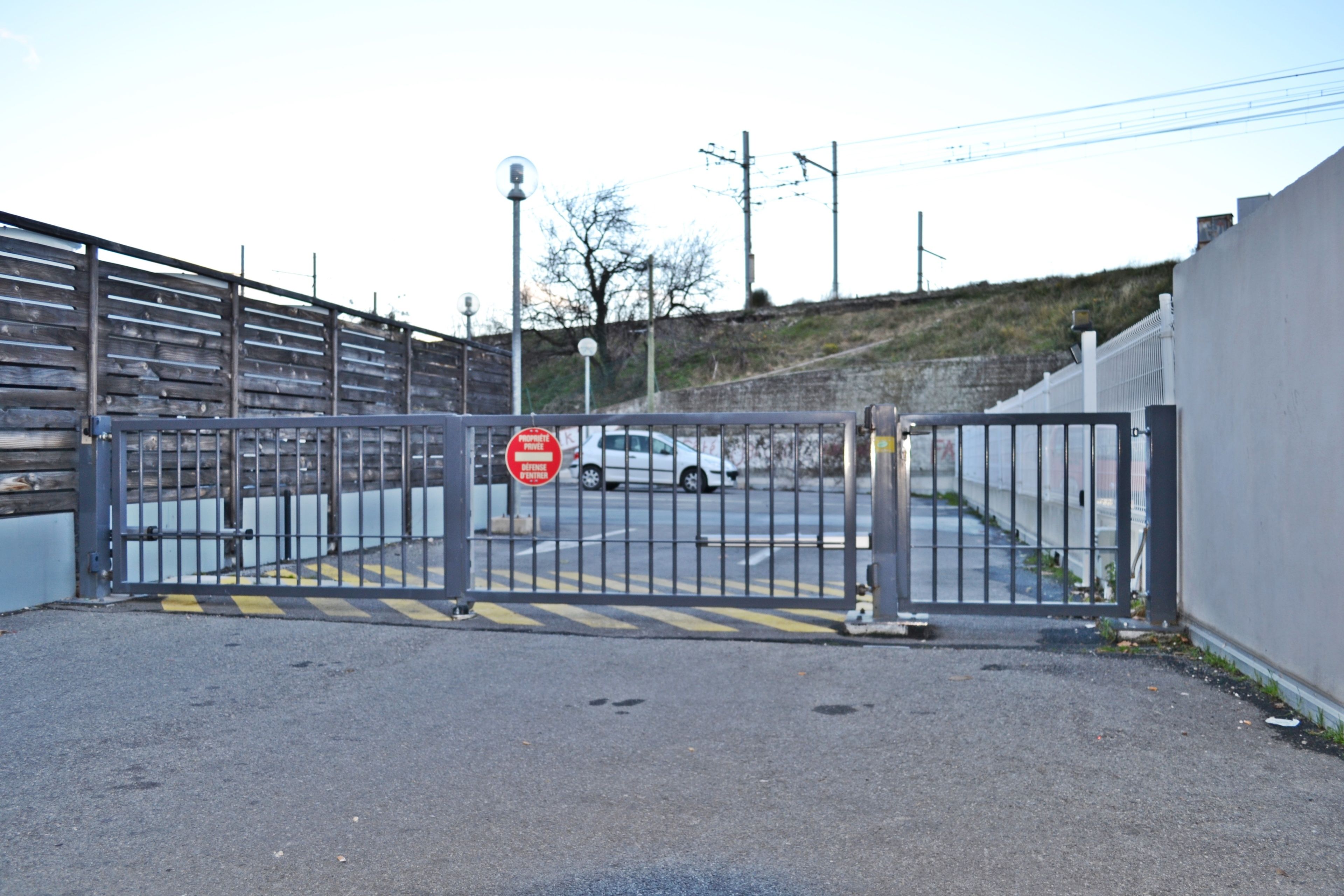 A gated entrance with a 'No Entry' sign, a metal fence, and a white car parked in the background.
