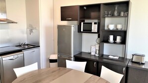 Een moderne keuken met een ingebouwde magnetron, koelkast en vaatwasser. Er staat een eettafel met stoelen en een koffiezetapparaat op het aanrecht.