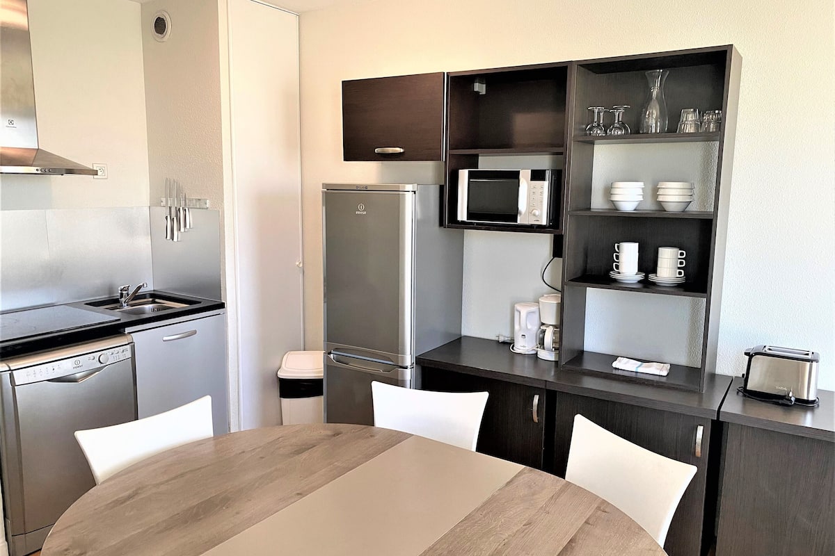 A modern kitchen with a built-in microwave, refrigerator, and dishwasher. There is a dining table with chairs and a coffee maker on the counter.