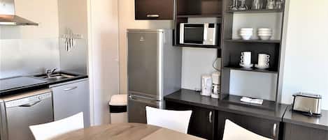 Una cocina moderna equipada con microondas, refrigerador y lavavajillas. Hay una mesa de comedor con sillas y una cafetera sobre la encimera.