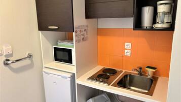Een kleine keuken met een magnetron, een koelkastje, een spoelbak en een koffiezetapparaat.