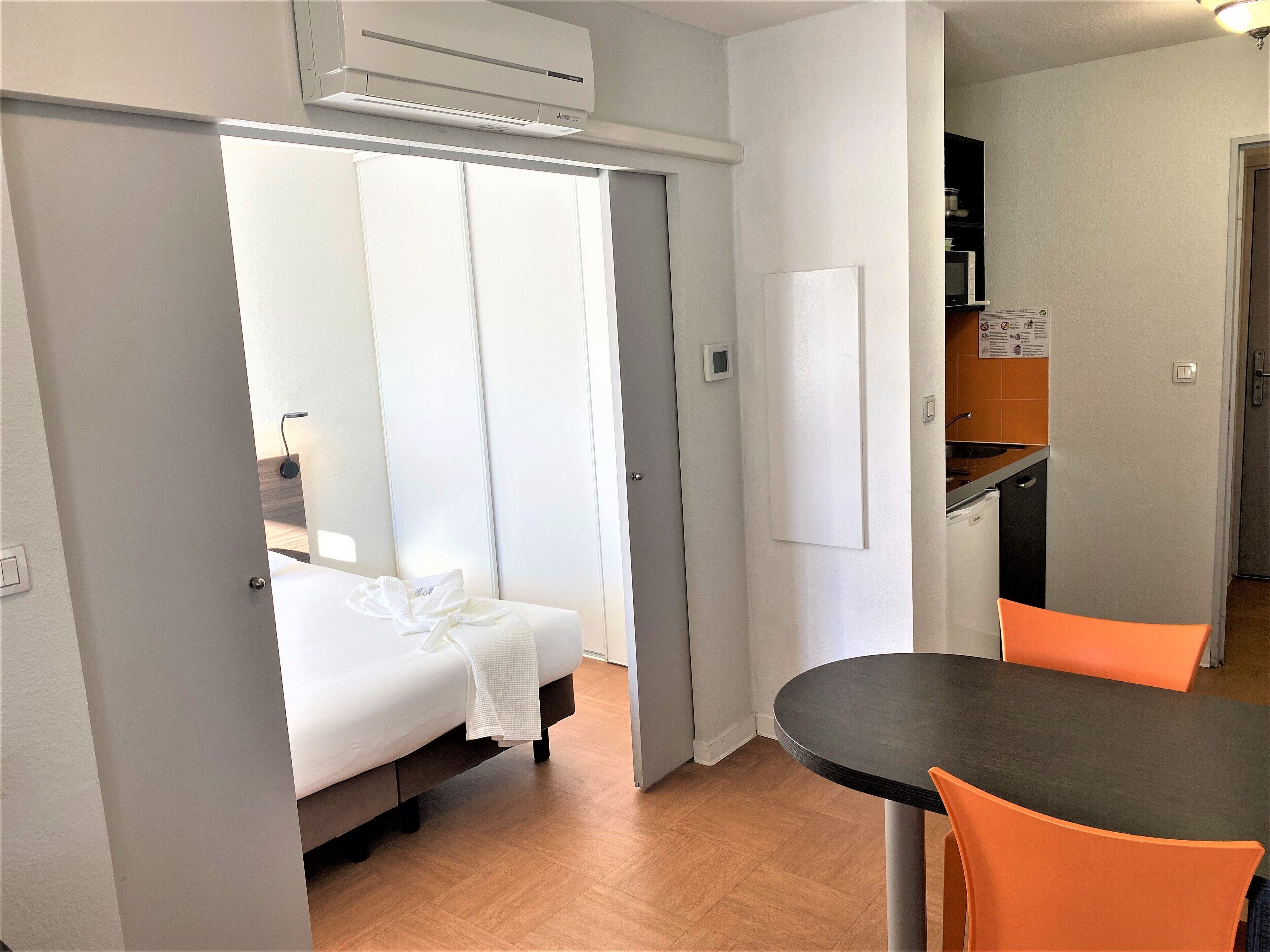 A hotel room with a bed, a table, and a kitchenette.