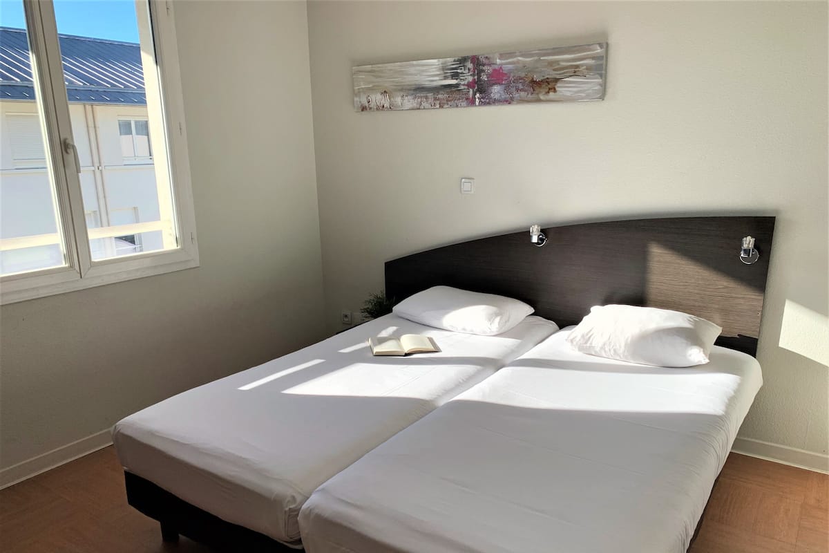 A double bed with white bedding, a bedside table, and a wall-mounted light fixture.