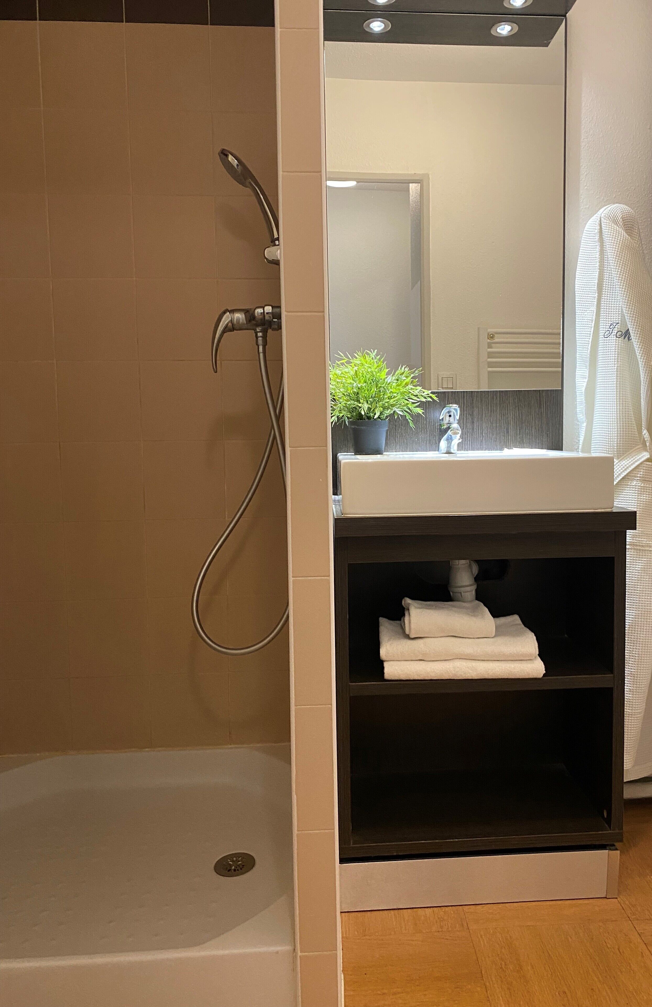 Une salle de bain avec une douche, un lavabo, un miroir et une étagère avec des serviettes.