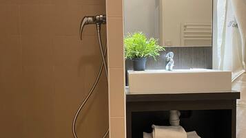 A bathroom with a shower, a sink, a mirror, and a shelf with towels.