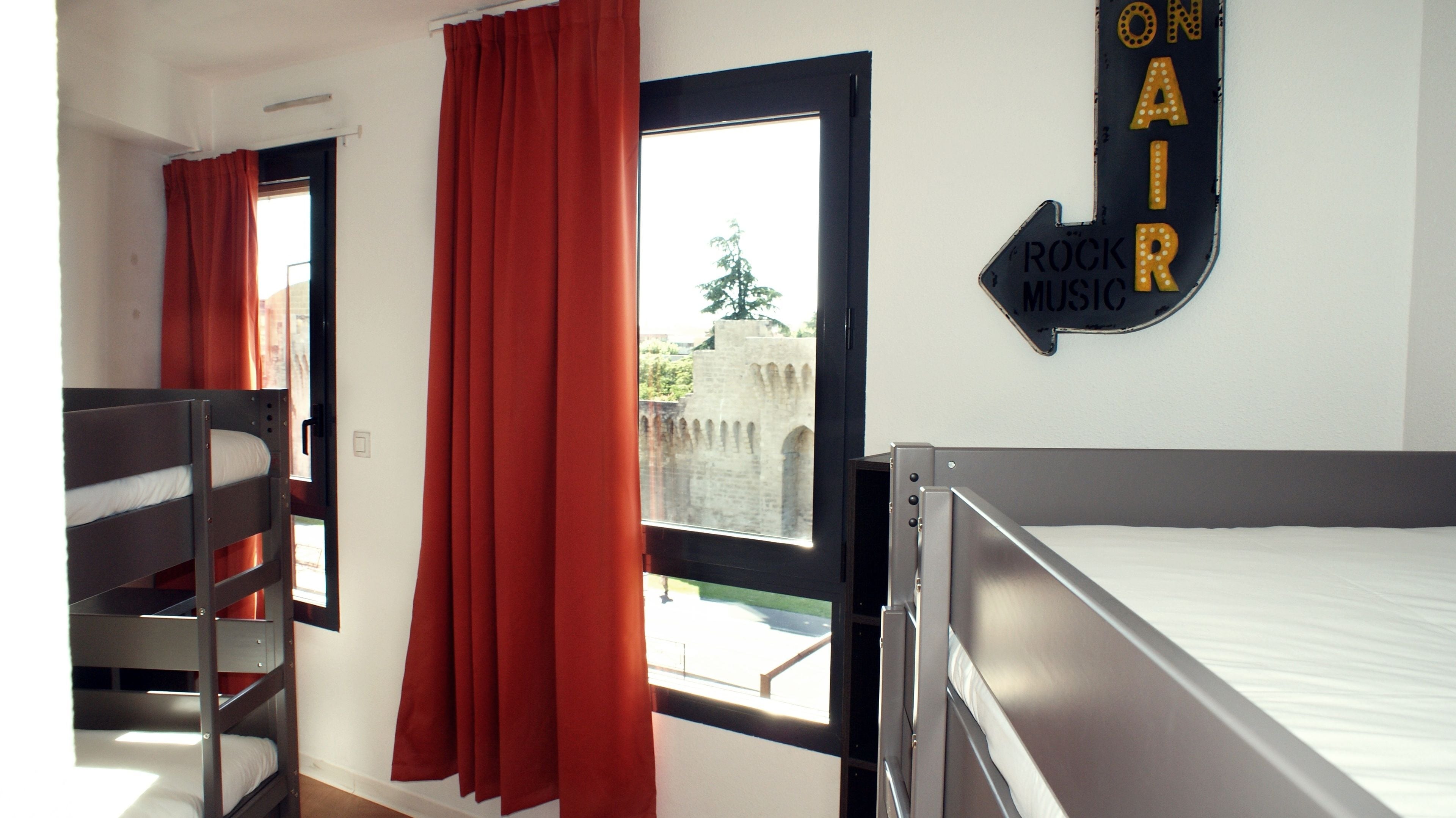 A dormitory room with bunk beds, a window with red curtains, and a wall sign that reads "ON AIR ROCK MUSIC".