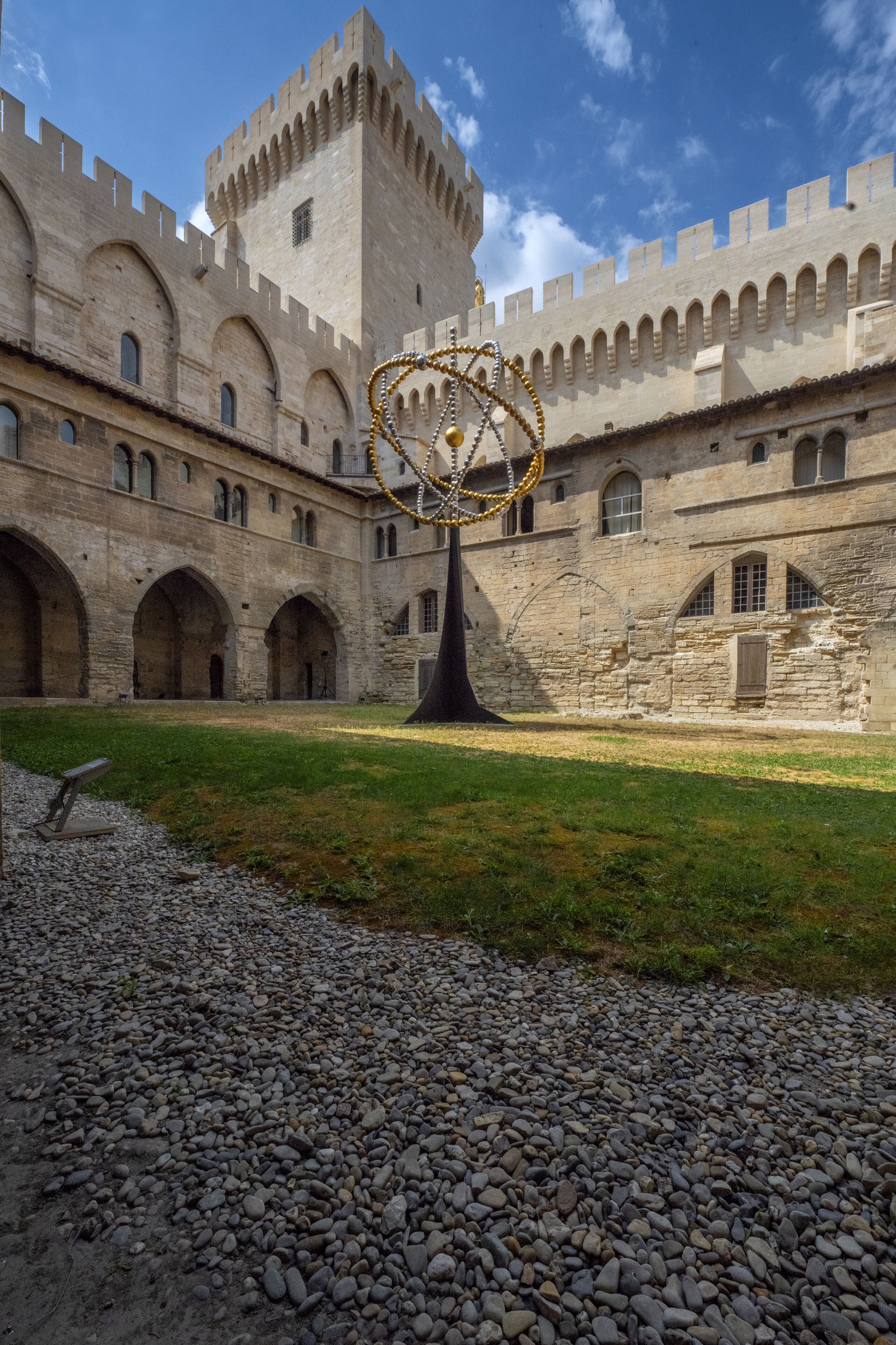 A courtyard with a large stone building featuring arched windows and a central tower.
