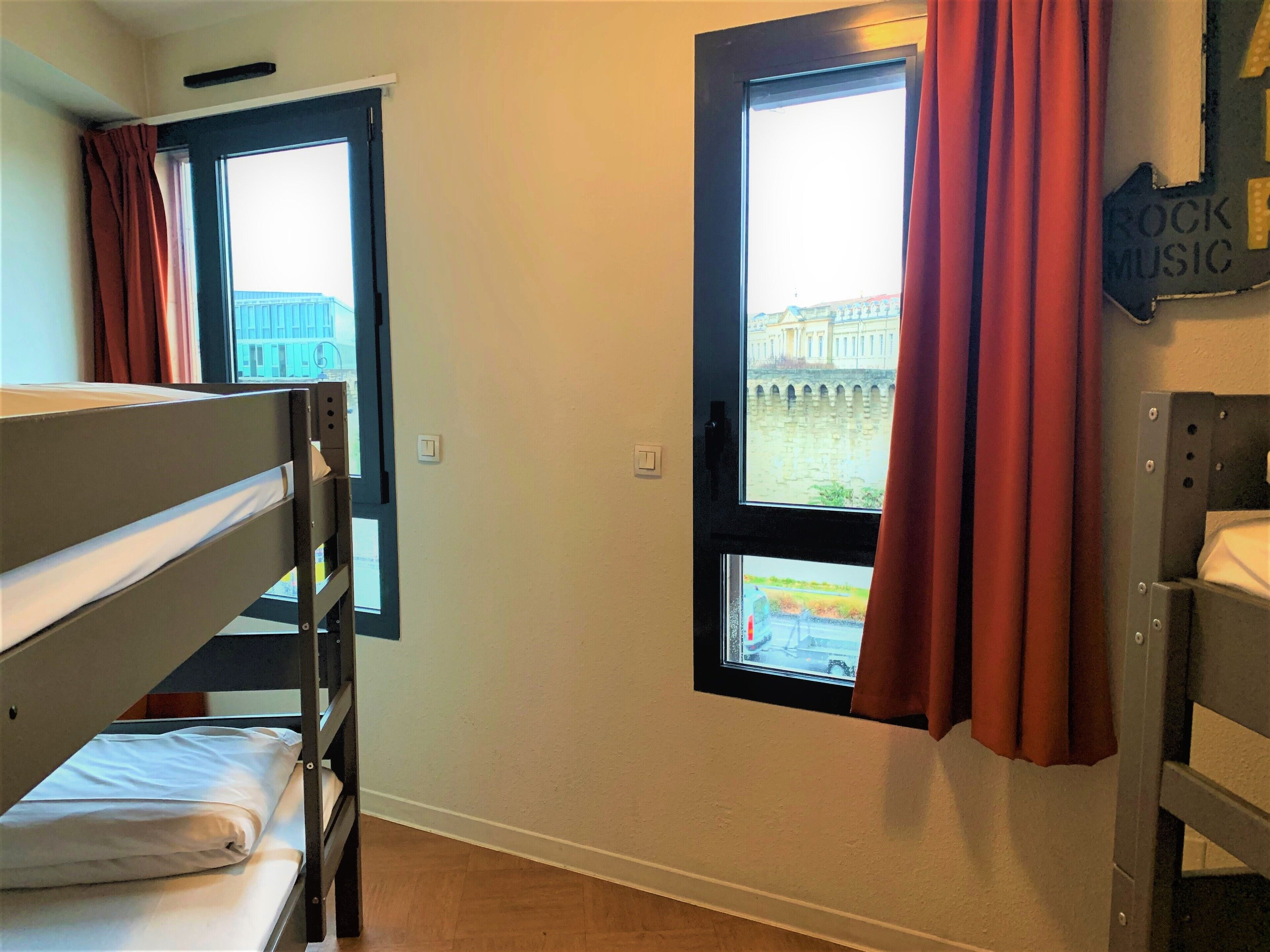 Un dormitorio con literas, una ventana con vista a un edificio y un letrero en la pared que dice 'ROCK MUSIC'.