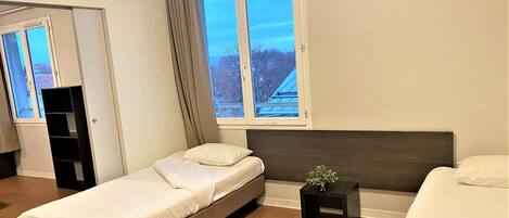 Une chambre à coucher moderne avec un lit simple, une table de chevet, une petite table avec une plante et une fenêtre avec des rideaux.