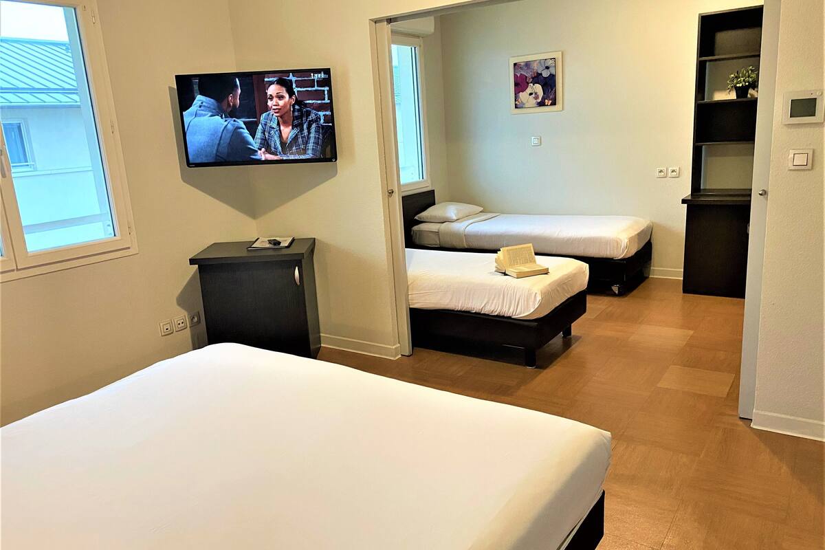 A hotel room with a large bed, two smaller beds, a TV on the wall, and a small desk.