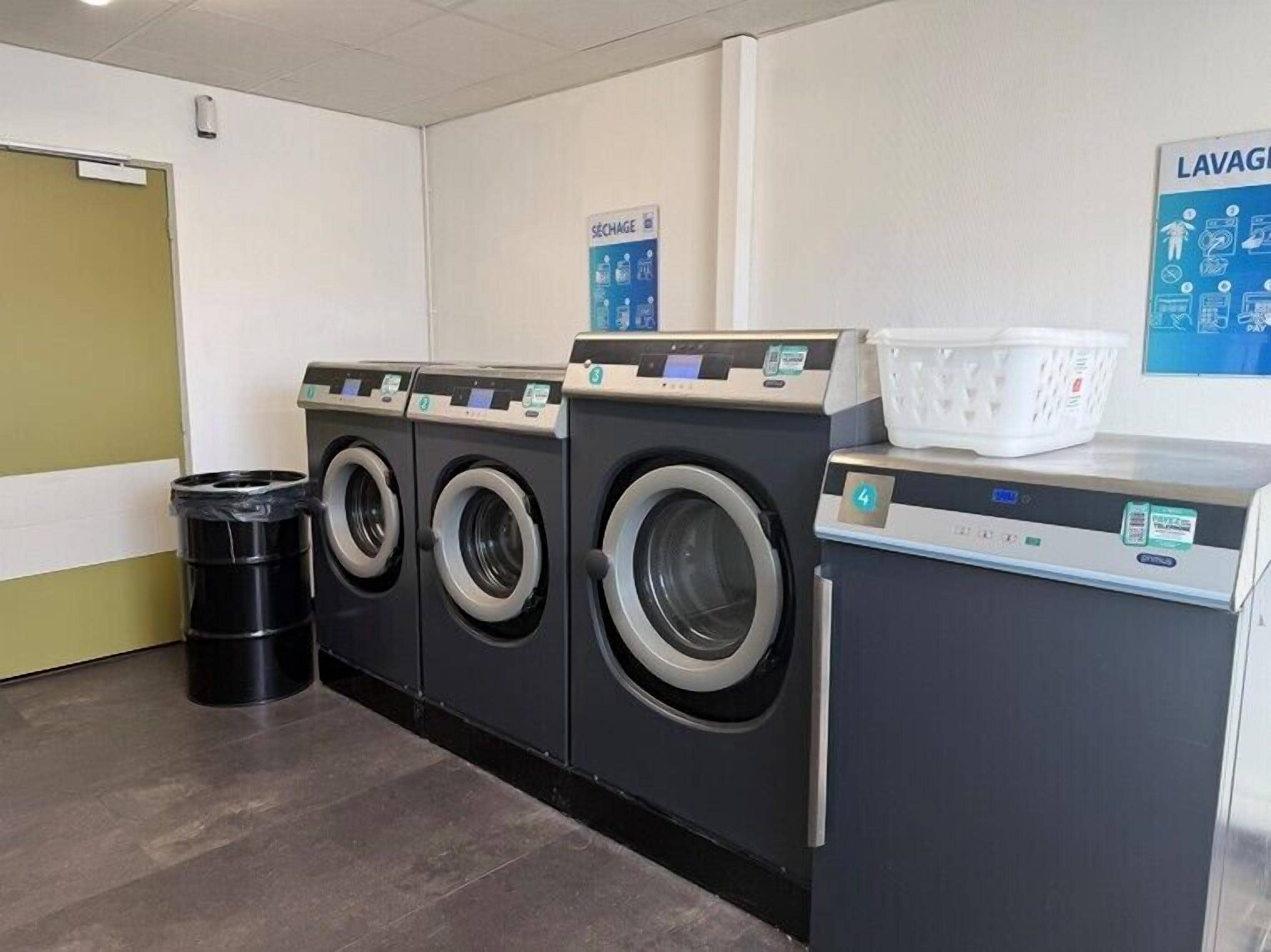 A laundry facility with four washing machines, a trash bin, and a laundry basket on the counter.