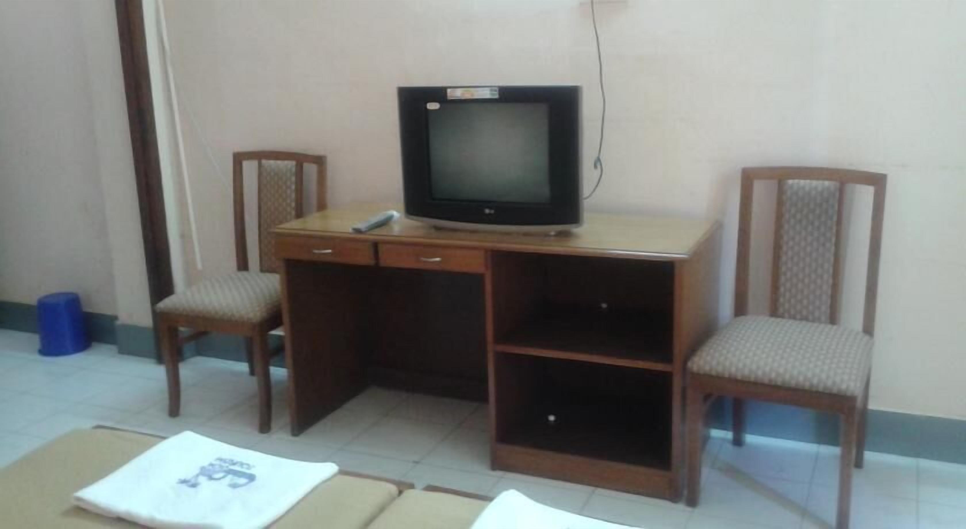 A room with a wooden desk, a television, two chairs, and a blue trash bin.