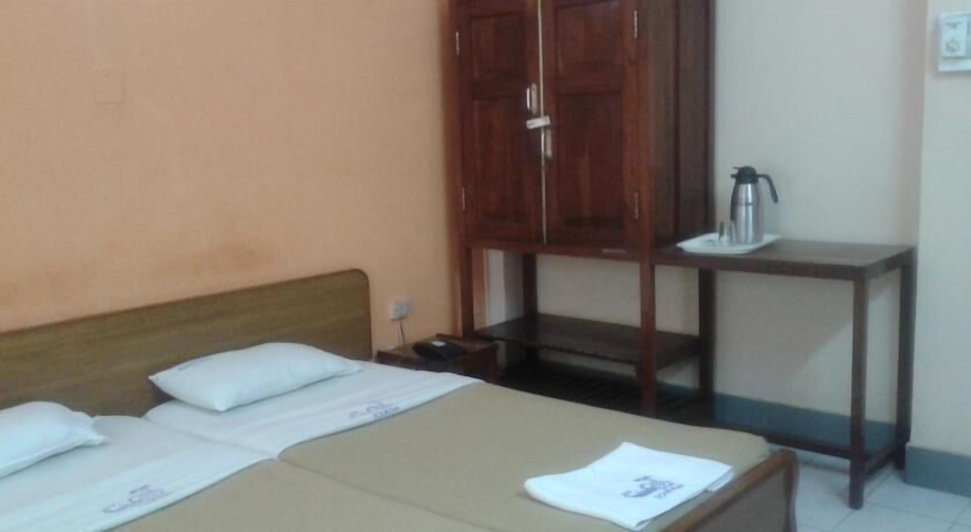 Une chambre avec deux lits, une armoire en bois et une petite table avec une bouilloire.