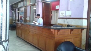 Un mostrador de recepción de madera, una recepcionista sentada y un separador de vidrio.