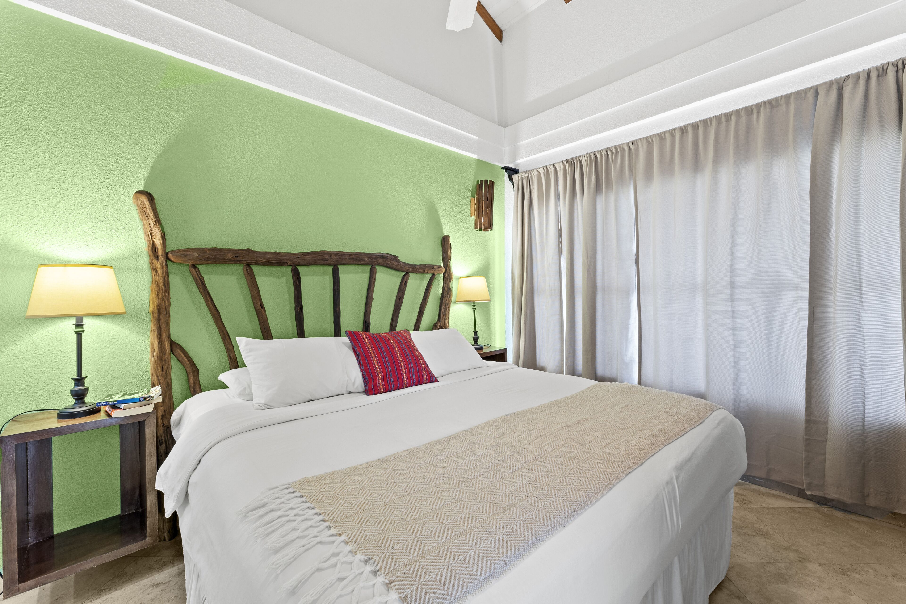 A neatly made bed with a white comforter and a beige throw, flanked by two bedside lamps on wooden nightstands.
