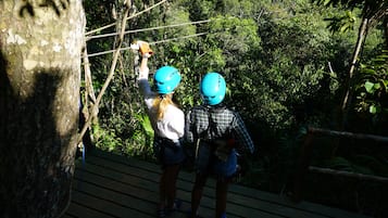 Duas pessoas em uma plataforma de madeira com uma ponte suspensa numa área arborizada.
