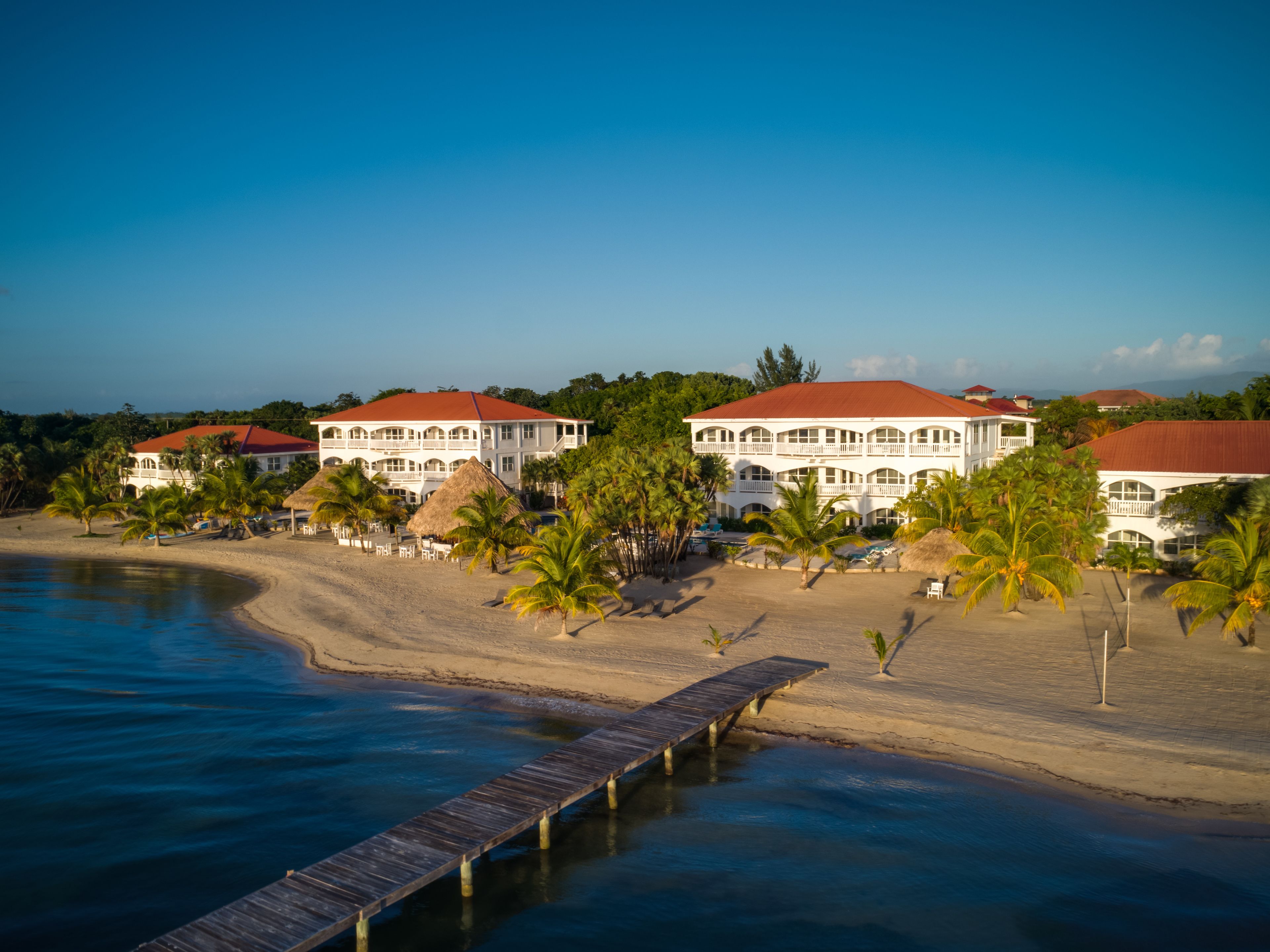 A beachfront hotel with multiple buildings, a wooden pier, and palm trees.