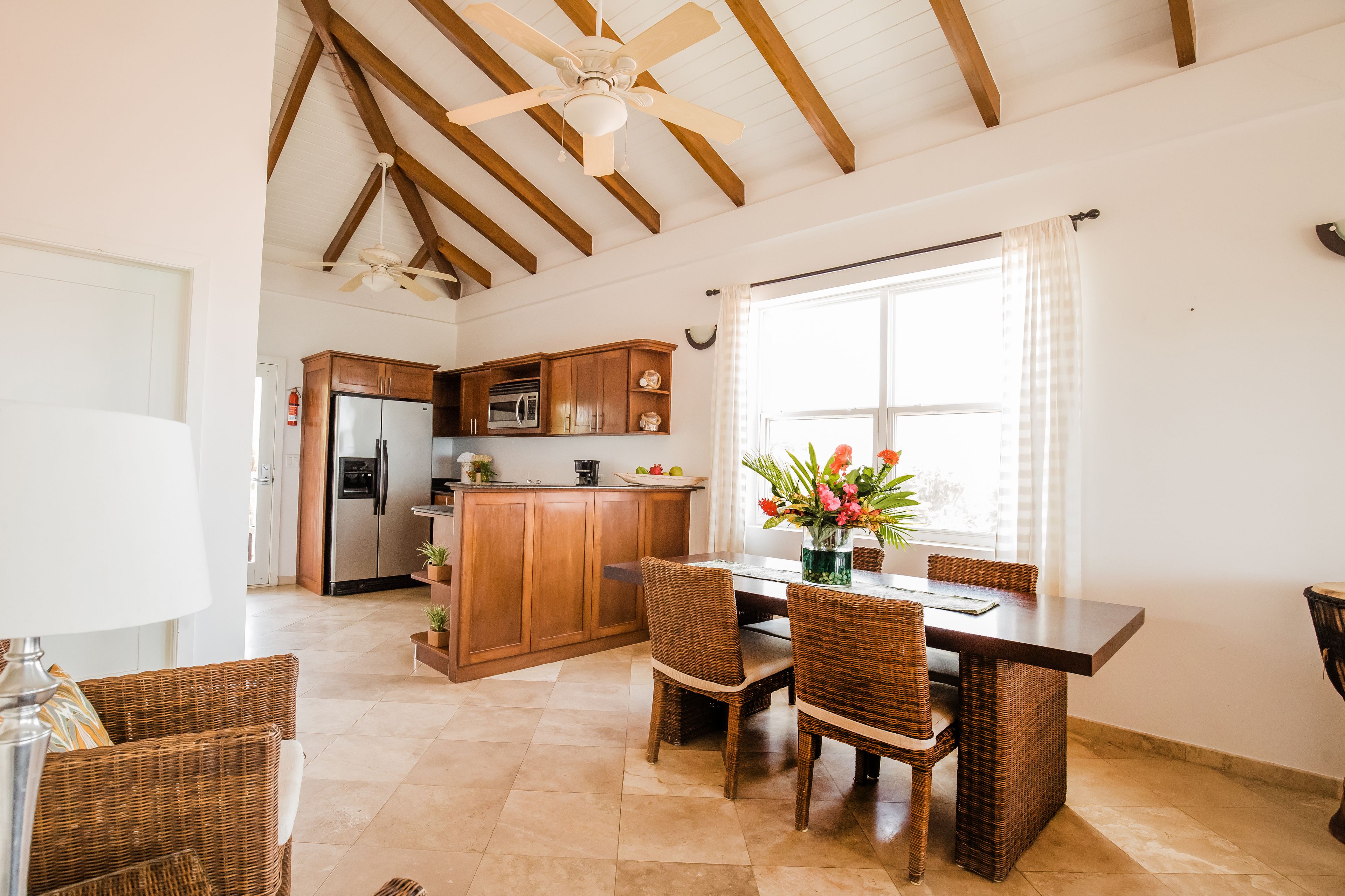 Una cocina amplia con armarios de madera, una isla central y una zona de comedor con sillas de mimbre.