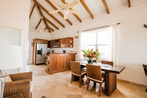 Una cocina amplia con armarios de madera, una isla central y una zona de comedor con sillas de mimbre.
