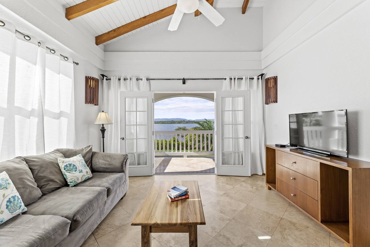 A living room with a sofa, a coffee table, a TV, and a view through an open door to the outside.