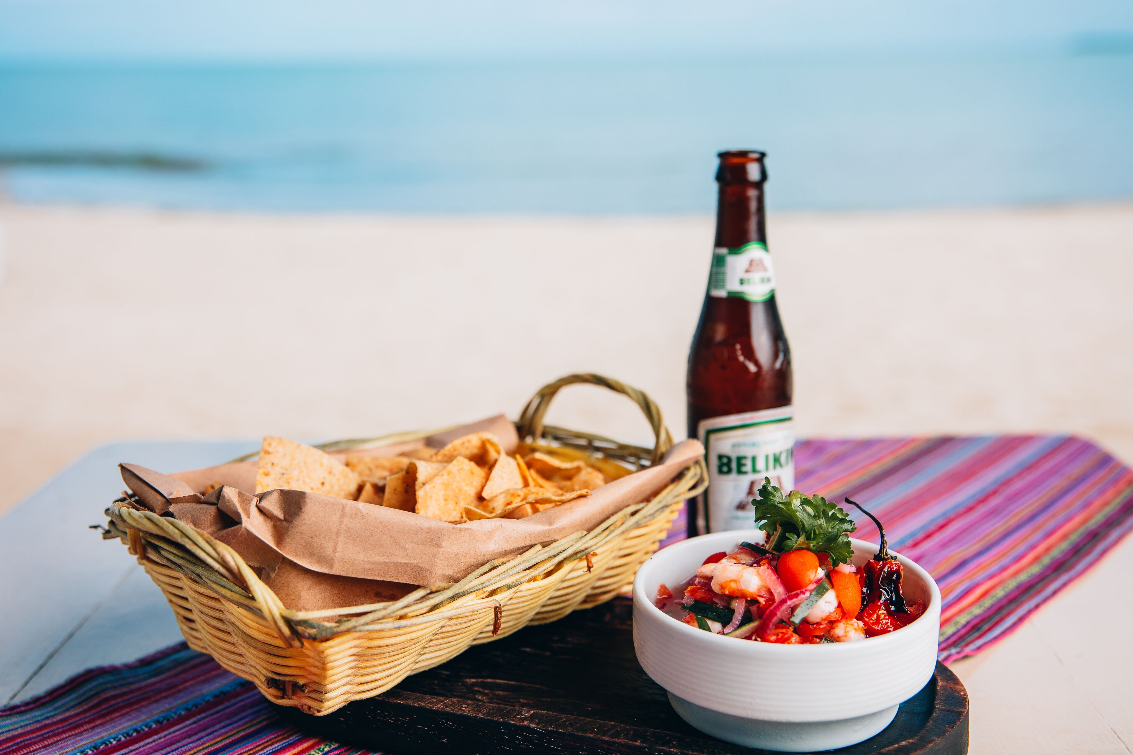 Ein Tisch am Strand mit einer Tüte Chips, einer Schüssel Salsa und einer Bierflasche.