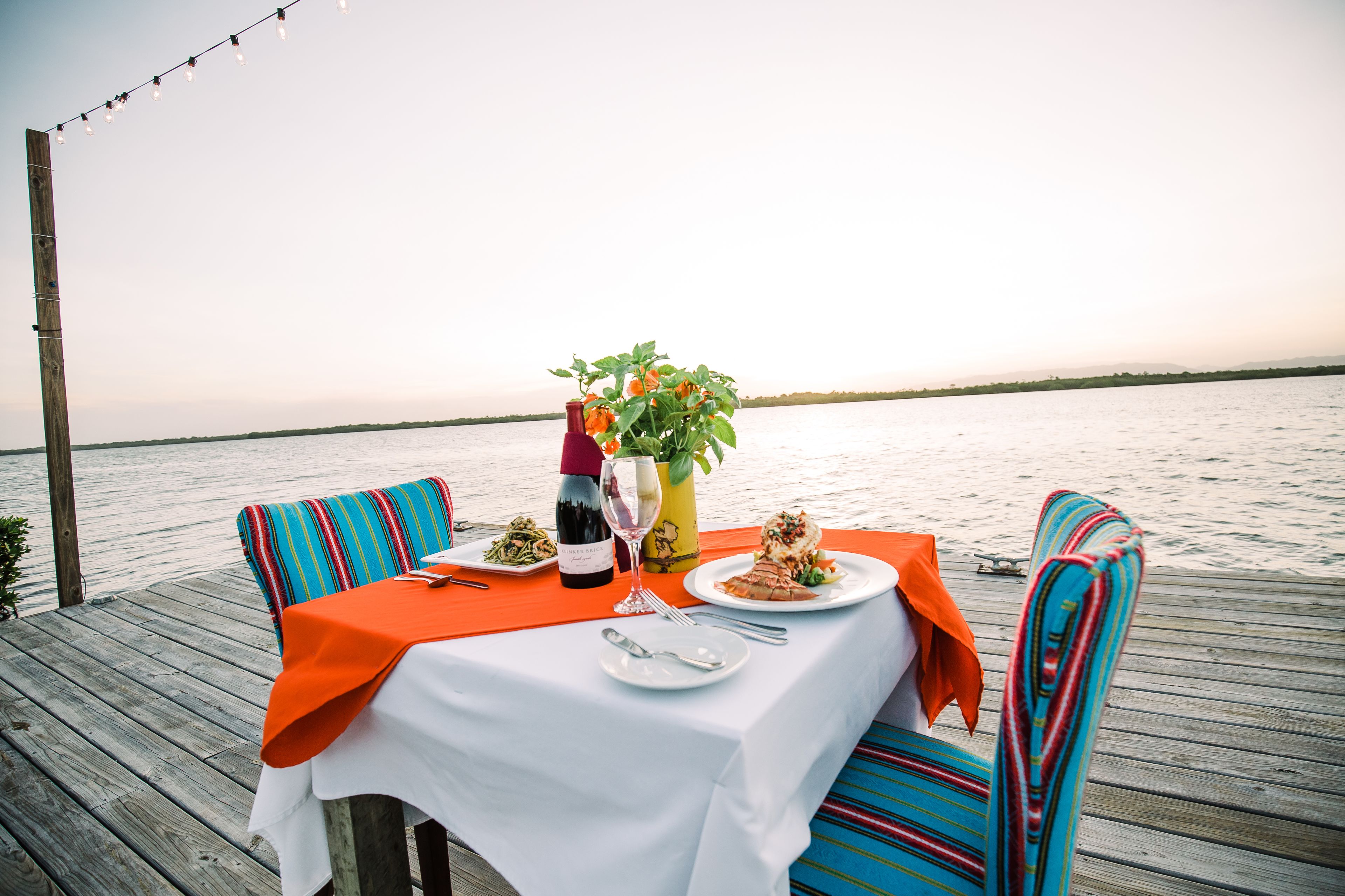 A table set with plates, cutlery, a bottle, and a glass, with a view of the water in the background.