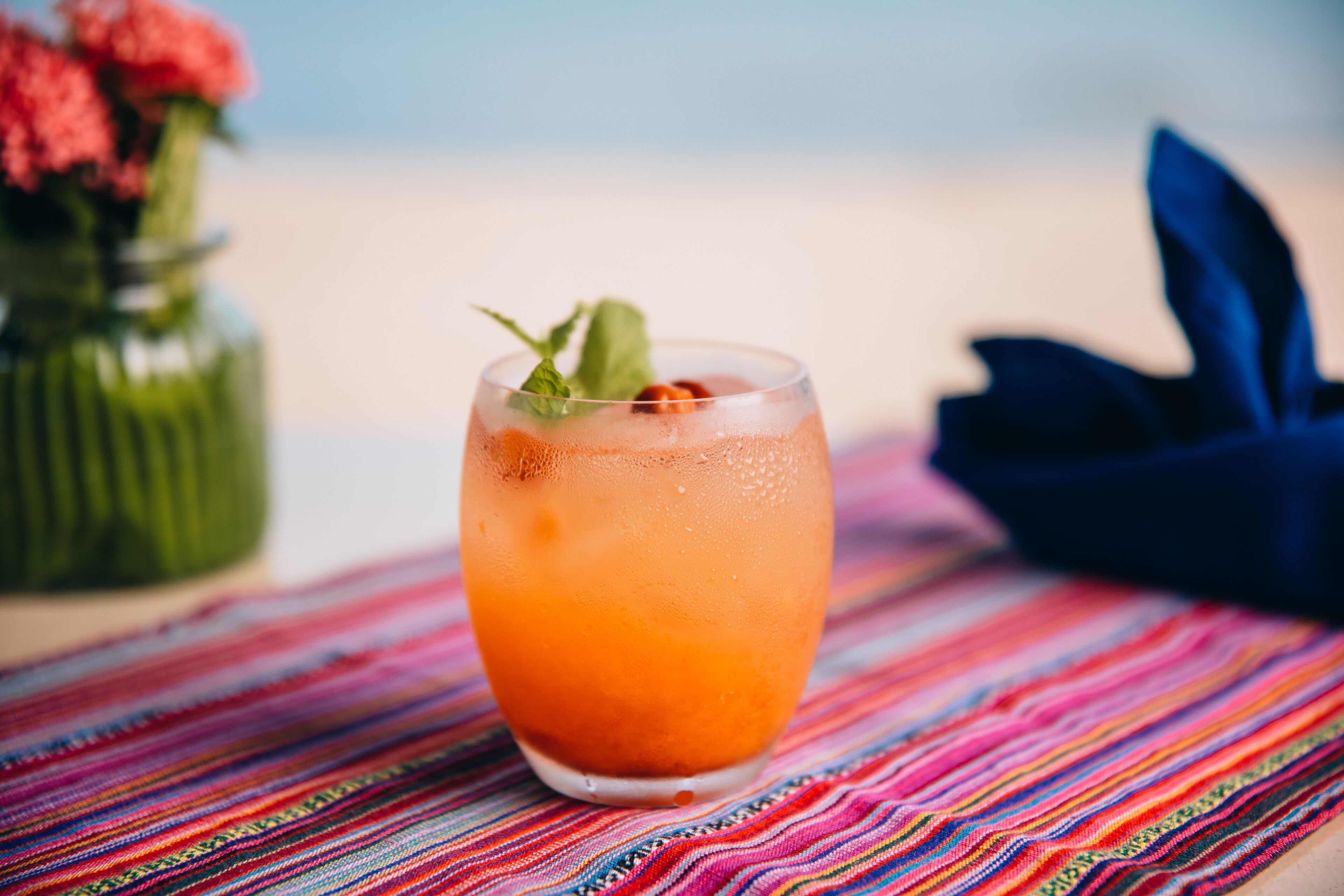 A glass of orange beverage with mint on a colorful striped tablecloth.