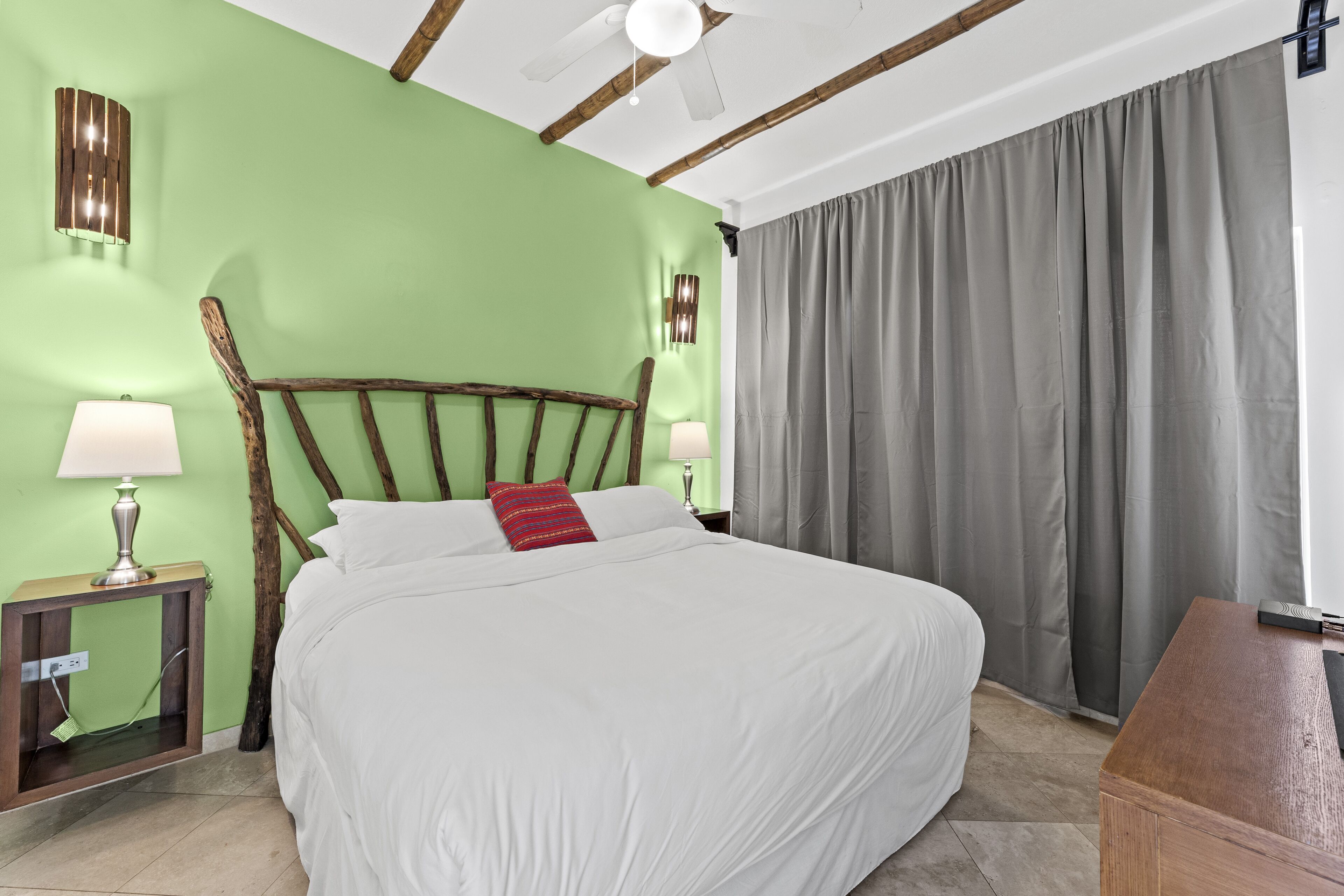 A neatly made bed with white linens and a red pillow, a wooden headboard, and a nightstand with a lamp.