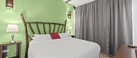 A neatly made bed with white linens and a red pillow, a wooden headboard, and a nightstand with a lamp.