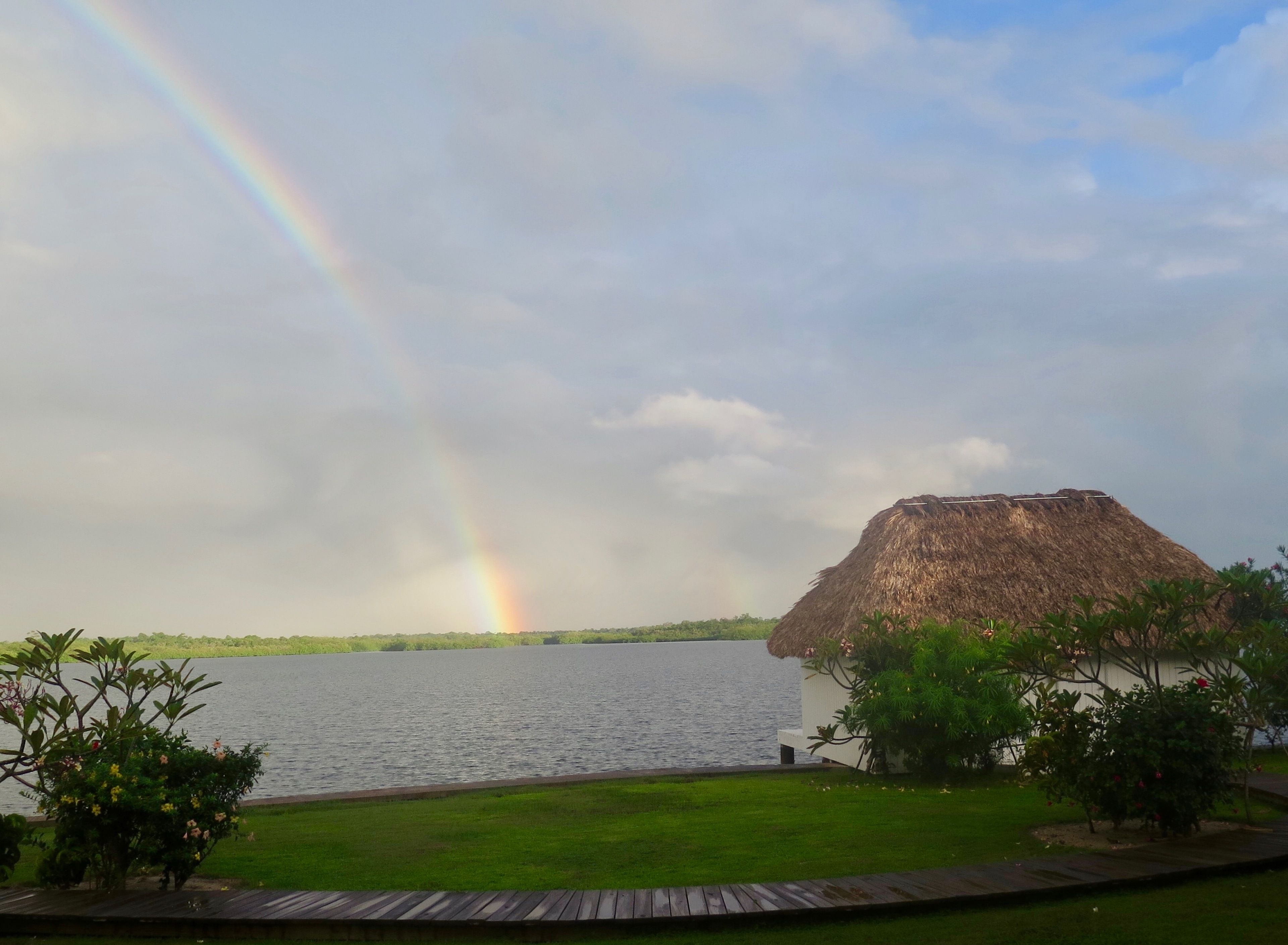 A thatched-roof structure by a lake with a rainbow.