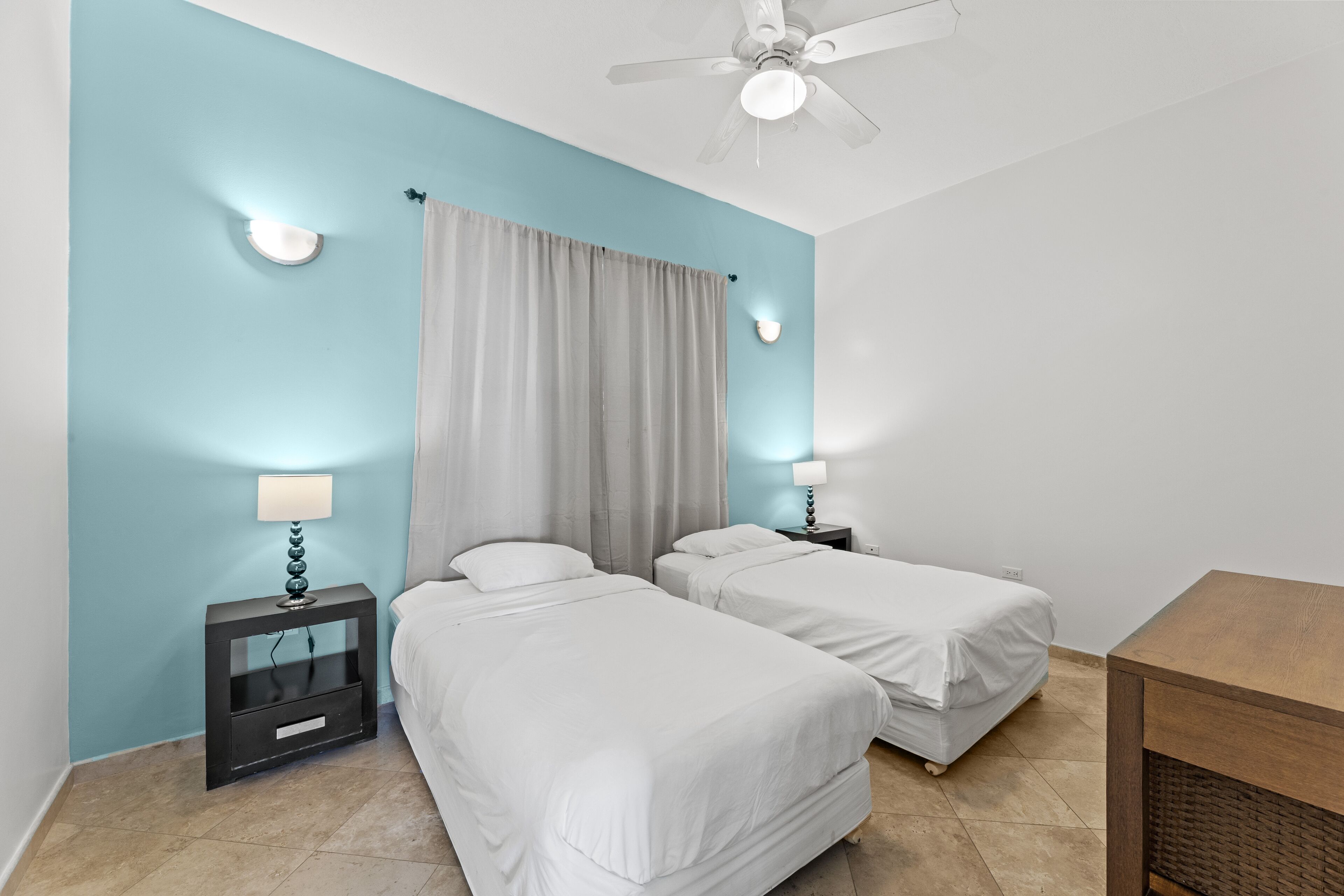 A room with two single beds, a ceiling fan, and a small table.
