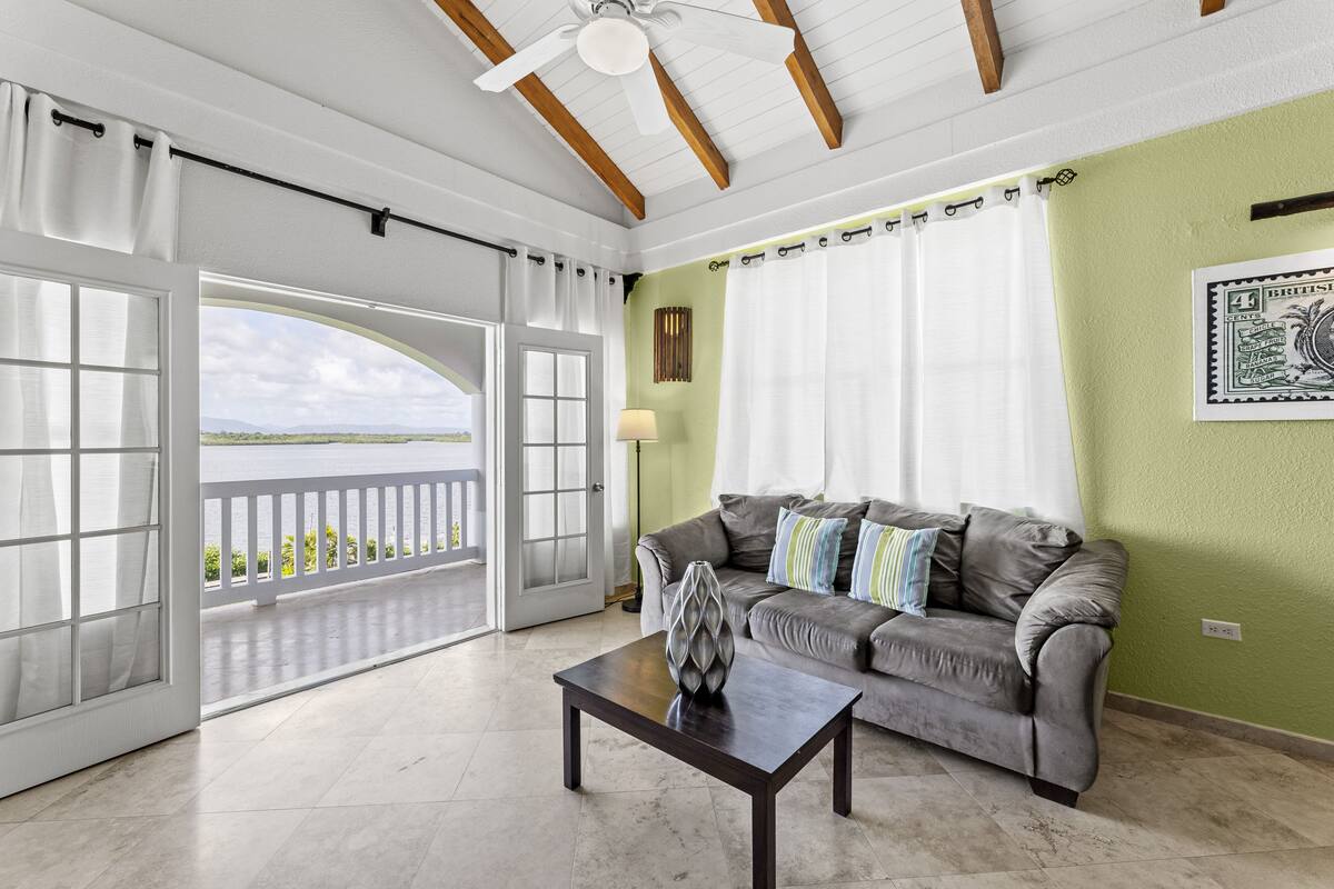 A spacious living room with a balcony, a grey sofa, and a table with a decorative vase.
