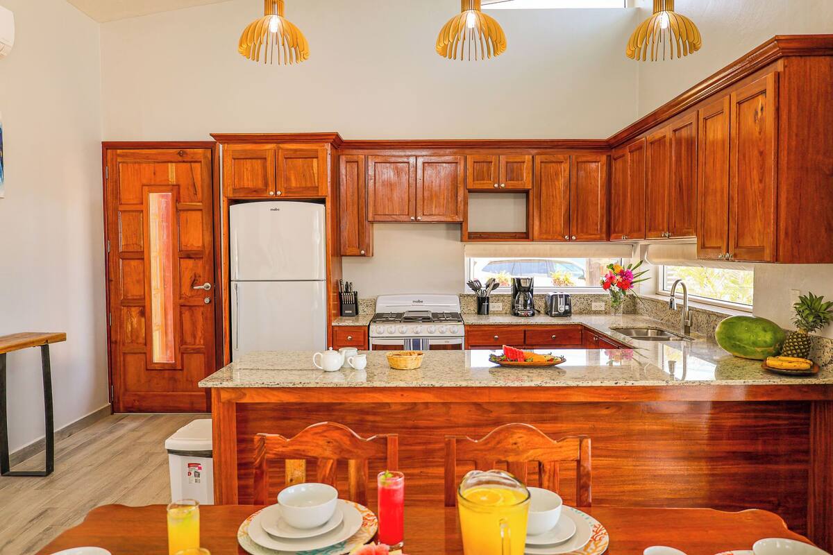 A kitchen with wooden cabinets, a refrigerator, a stove, and a dining area with a table set for two.