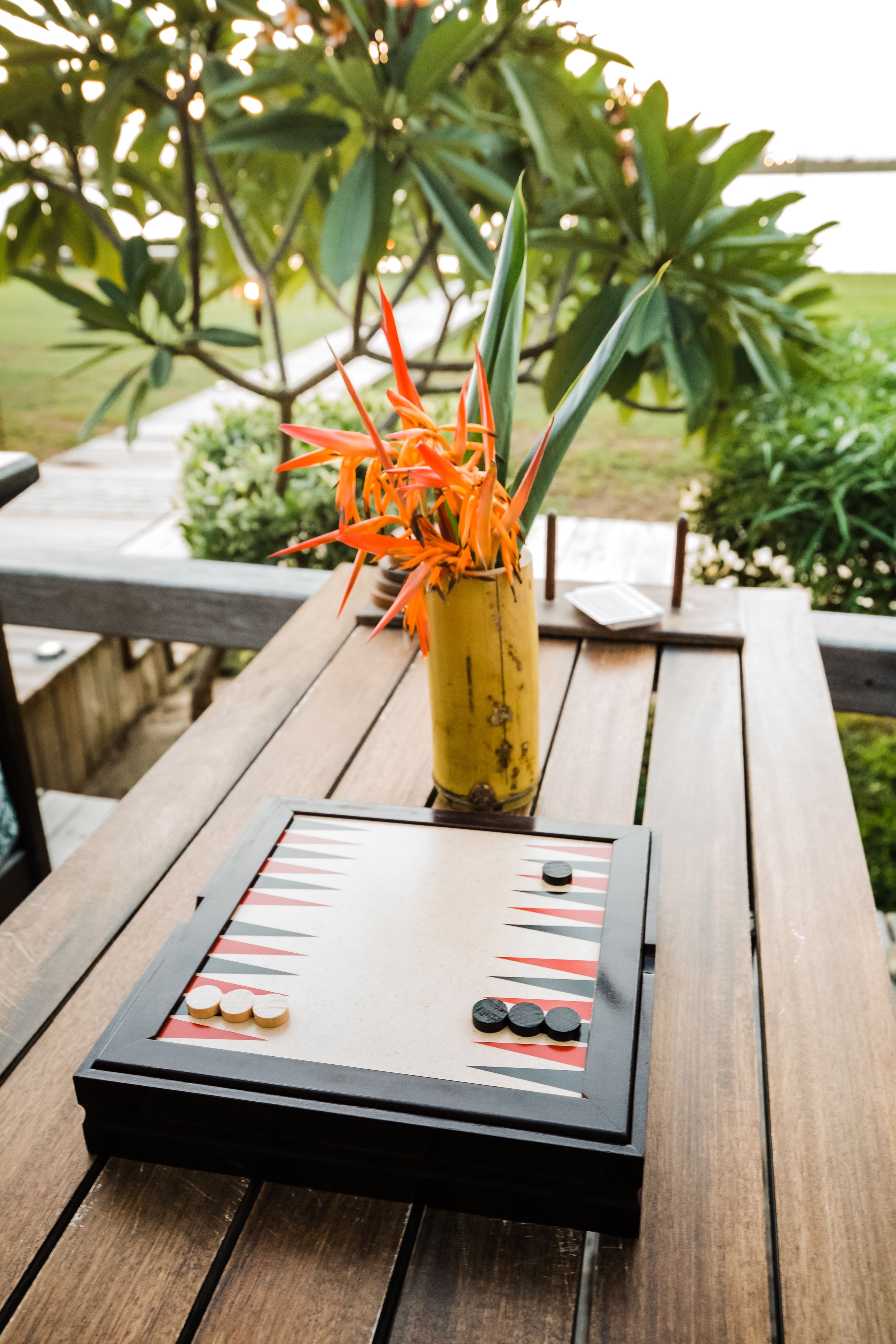 A wooden table with a game board and a yellow vase with orange flowers.