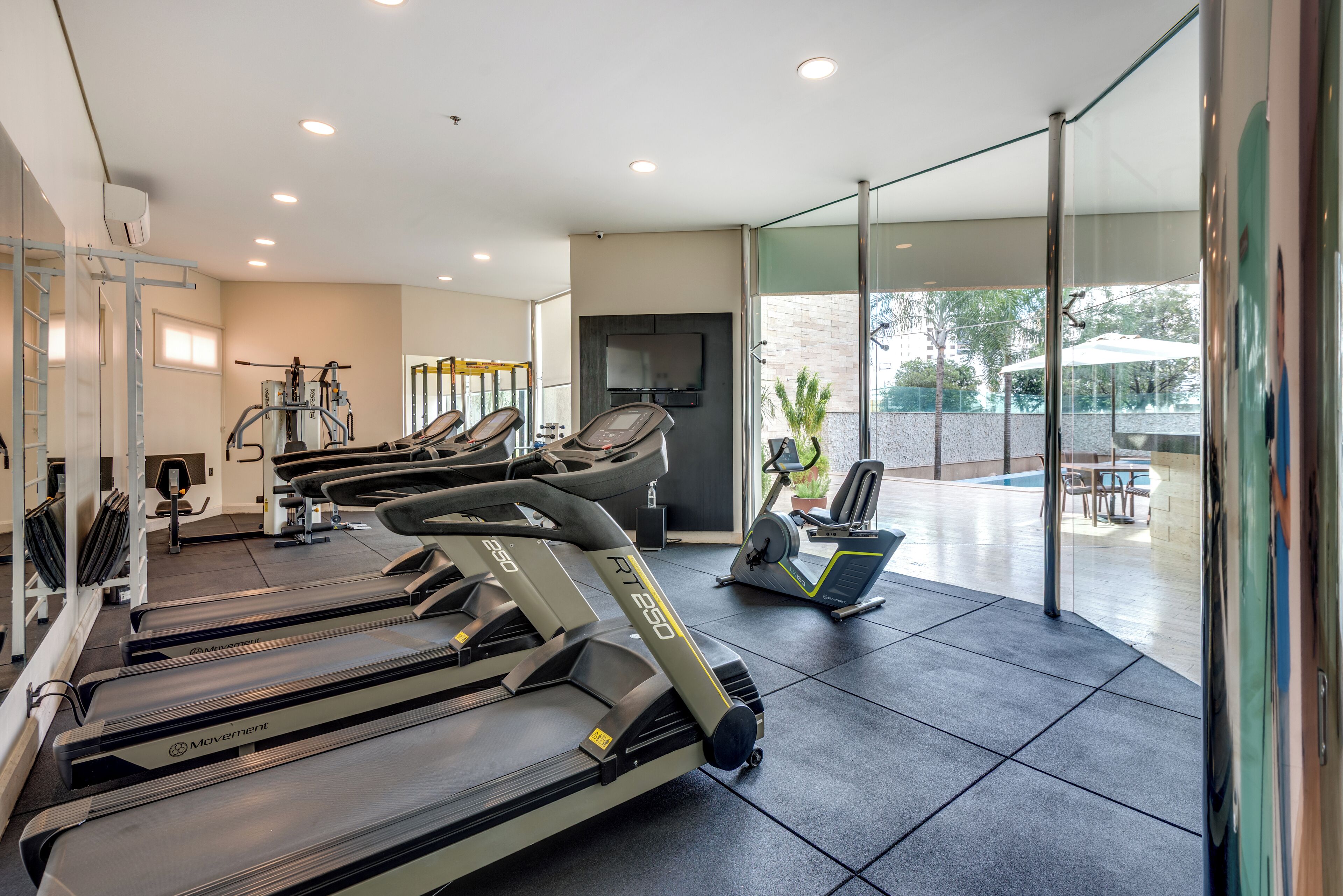 A gym with treadmills, stationary bikes, and a TV screen.
