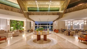 A spacious lobby with a central round table, multiple seating areas, and a view of the outdoor garden.