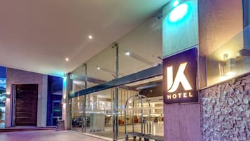 A hotel entrance with a modern design, featuring a glass facade and a prominent illuminated sign.