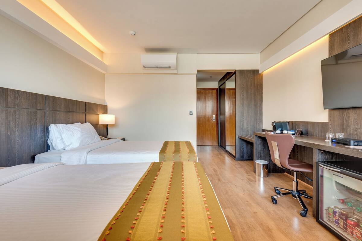 Habitación de hotel con dos camas, un escritorio, una silla, un televisor y un minibar.