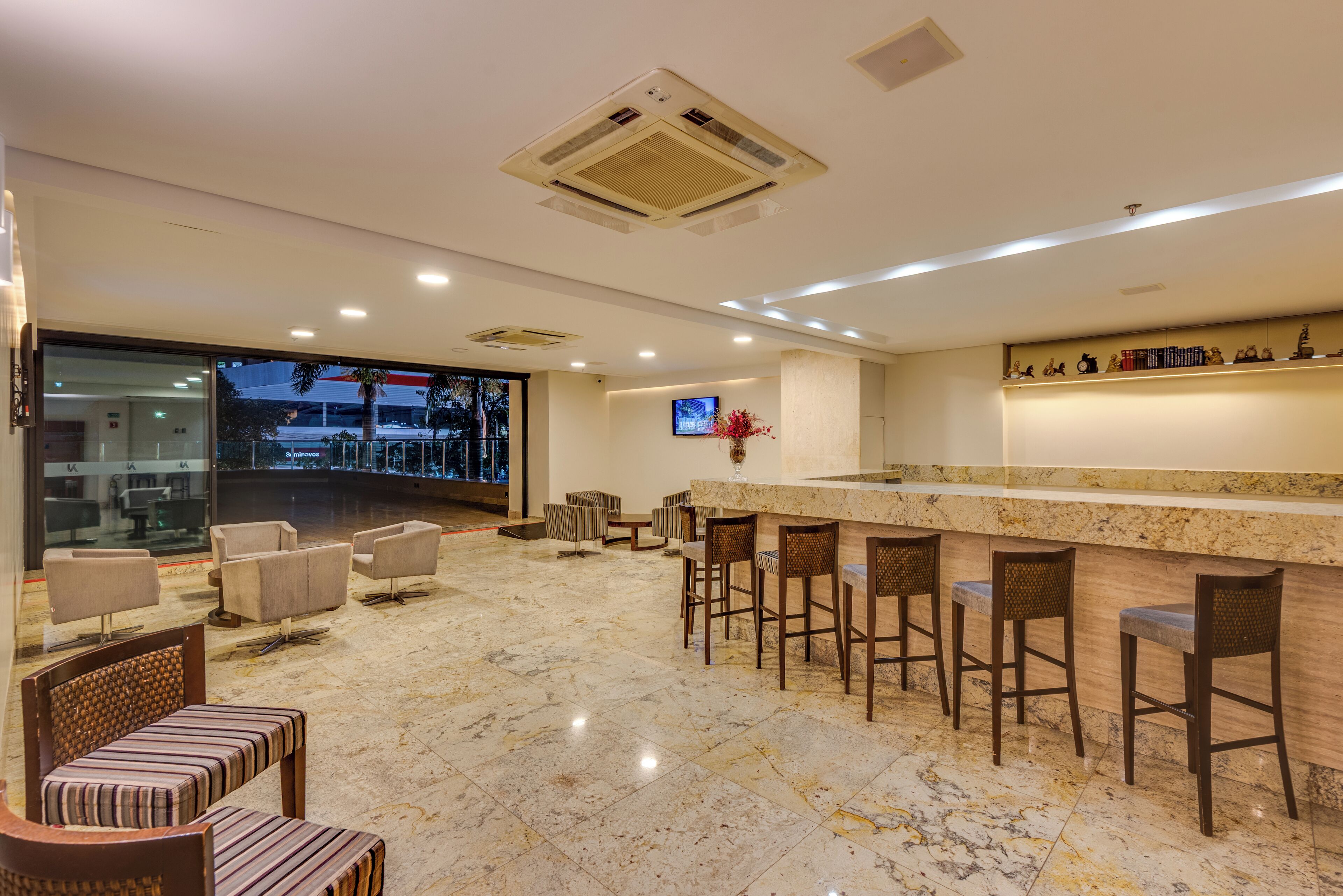 Un hall de hotel con piso de mármol, zona de estar y un bar con taburetes.