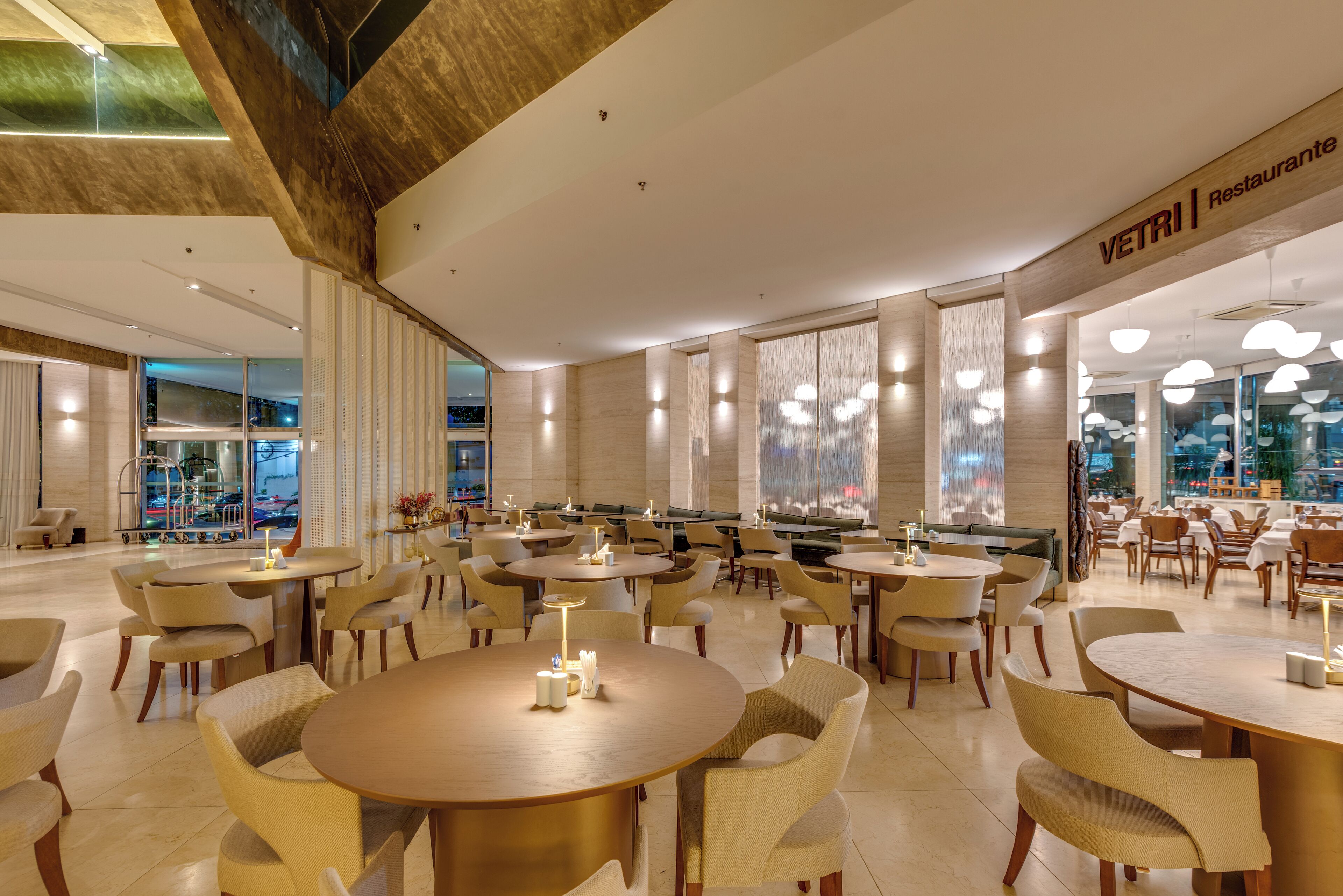 Un restaurante moderno con mesas y sillas redondas, un techo alto y ventanas amplias.