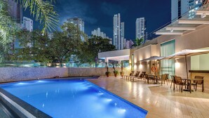 A swimming pool with a cityscape view, outdoor seating, and modern architecture.