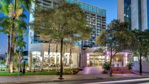 A modern hotel with a glass facade, outdoor seating, and a well-maintained garden.