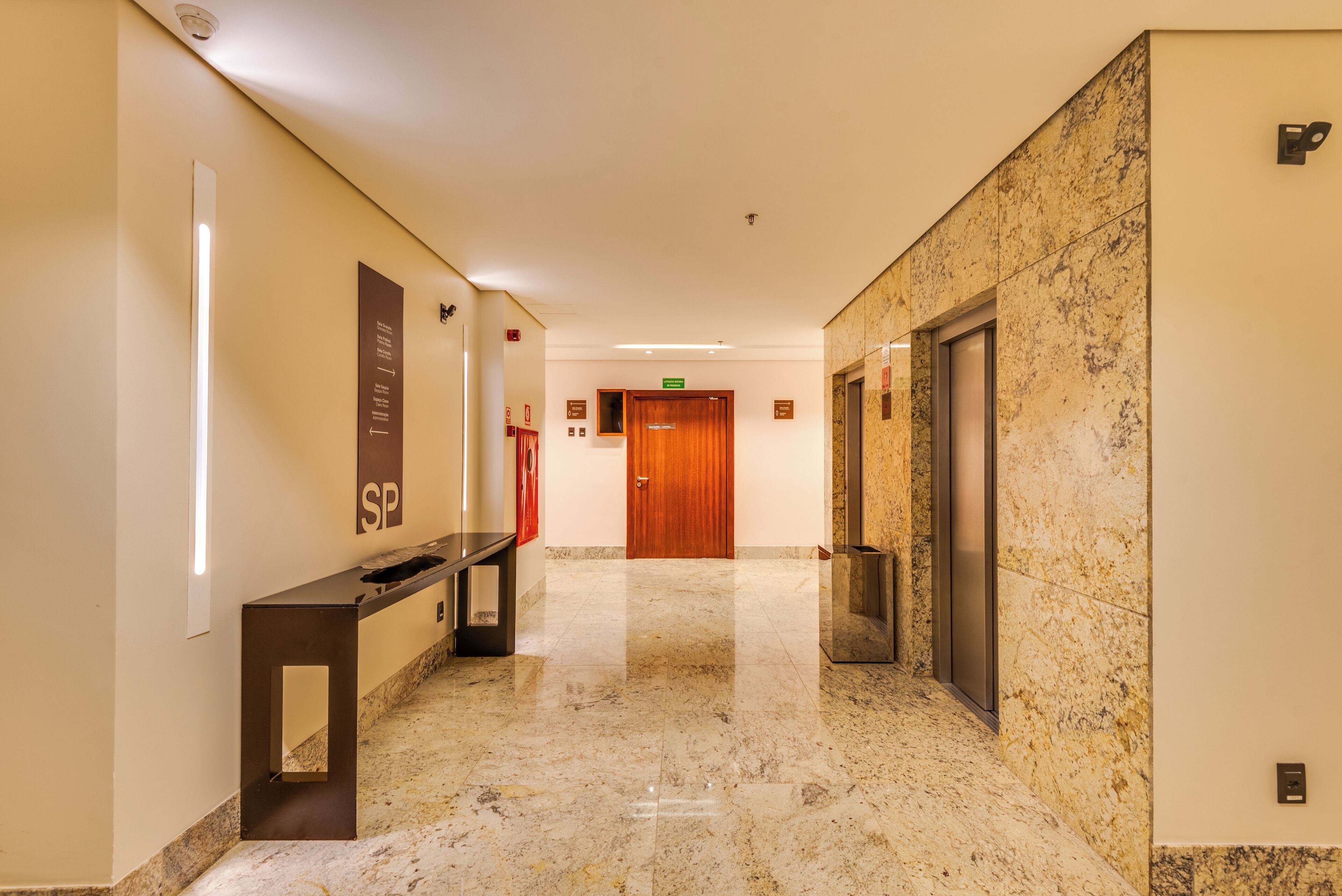 Un moderno vestíbulo de hotel con suelo de mármol, una recepción, una puerta de madera y un ascensor.