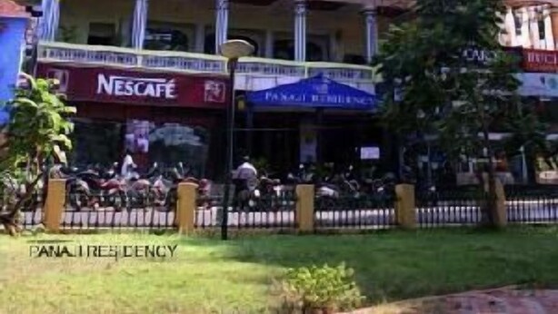 Un hotel de varios pisos con fachada amarilla, balcones en cada planta y una cafetería Nescafé a nivel de calle.