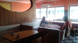 A restaurant with booths and tables, a large window with a view, and an air conditioning unit on the wall. - Margao Residency (Margao)