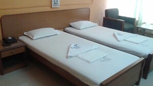 Habitación de hotel con dos camas individuales, cada una con una almohada y una toalla doblada con cuidado. Se observa una mesita de noche con un teléfono y un cajón pequeño.