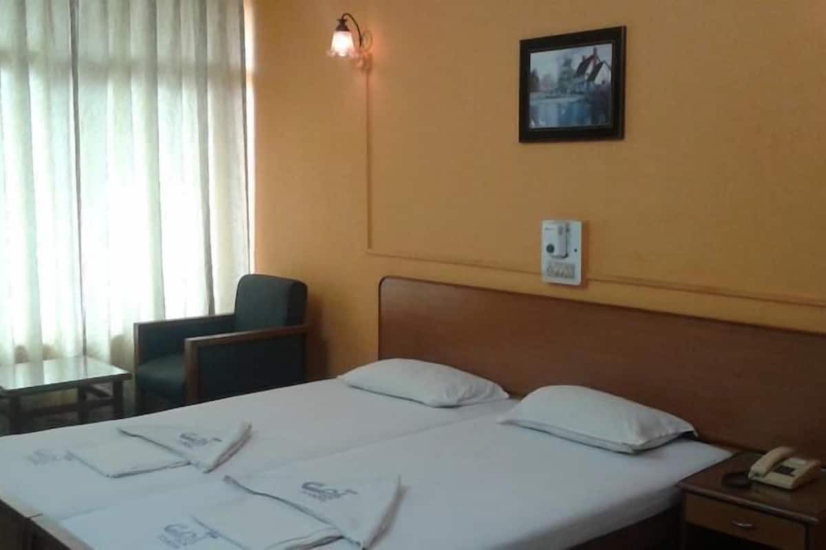 A hotel room with a double bed, a bedside table with a phone, a chair, a small table, and a window with curtains.